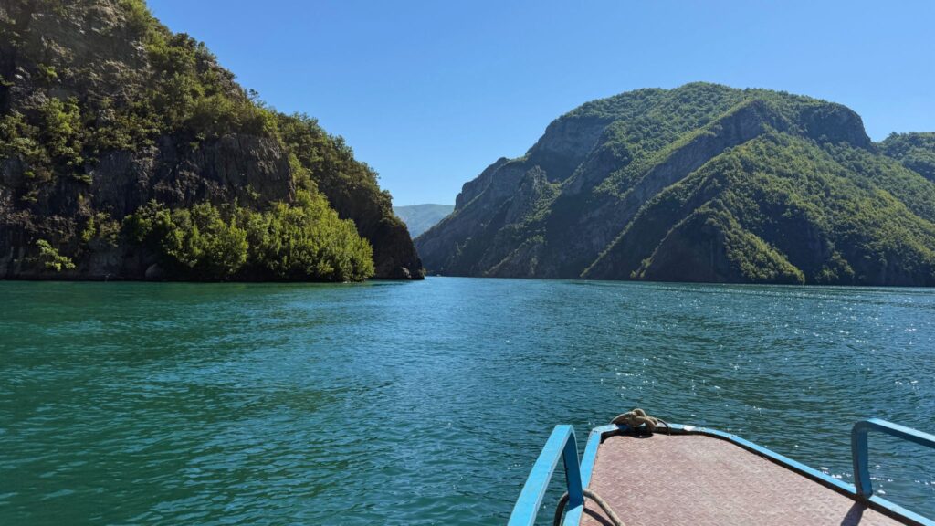 Boat journey through Lake Komani in Albania surrounded by steep green mountains