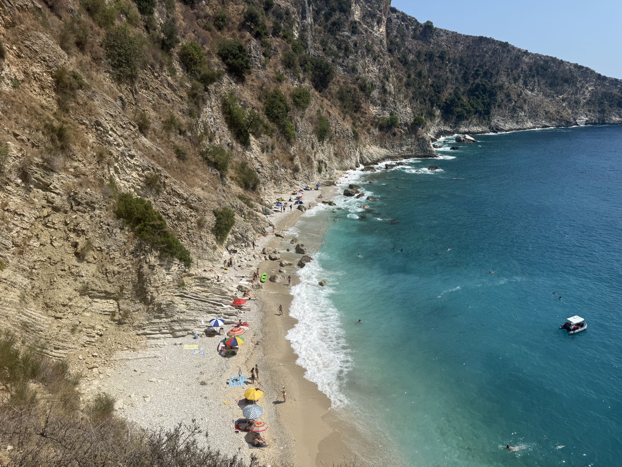 Aerial view of secluded beach cove with turquoise waters and rocky cliffs along Mediterranean coastline.