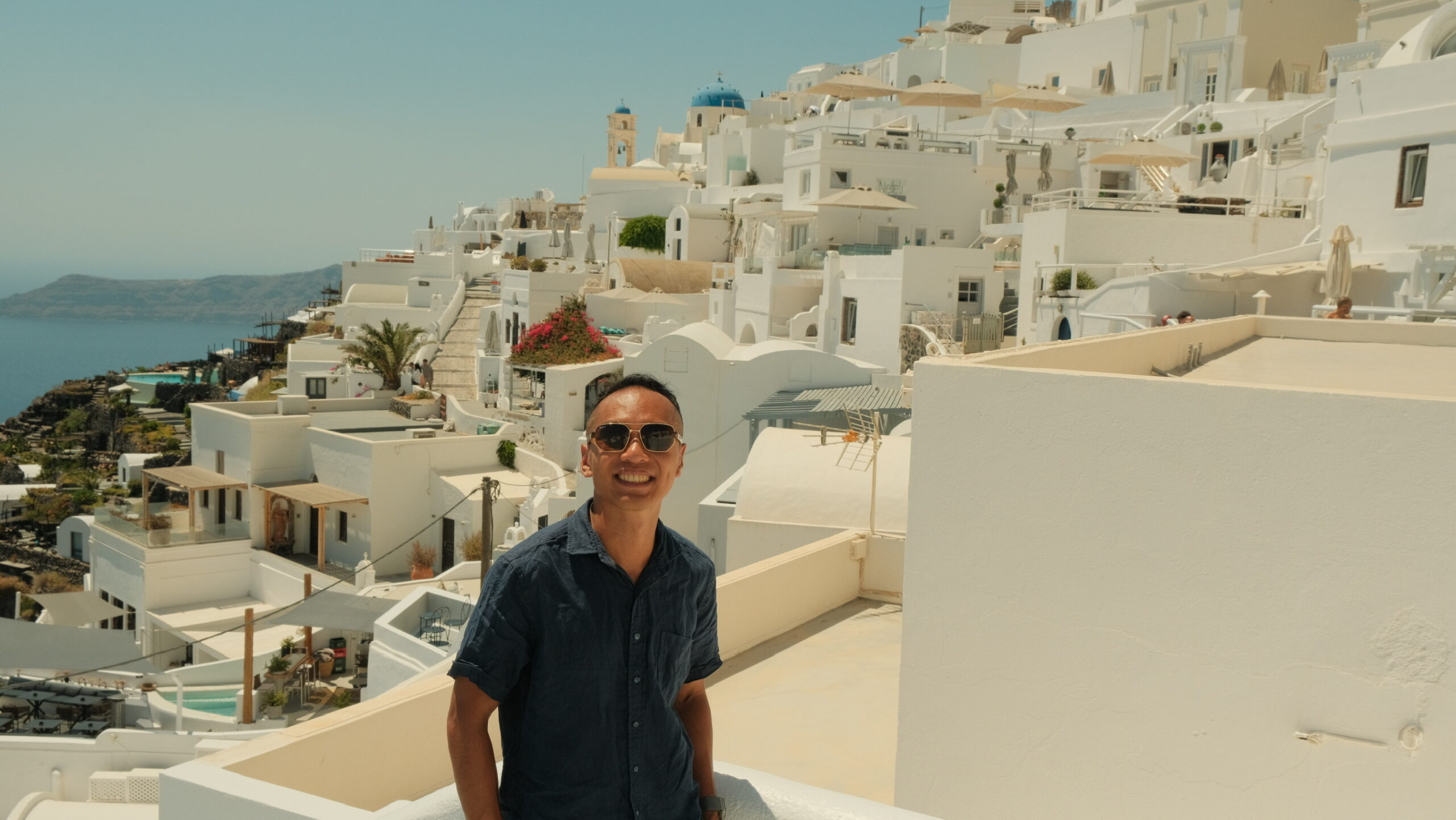 Man posing in front of iconic white-washed buildings and blue sea in Santorini, Greece.