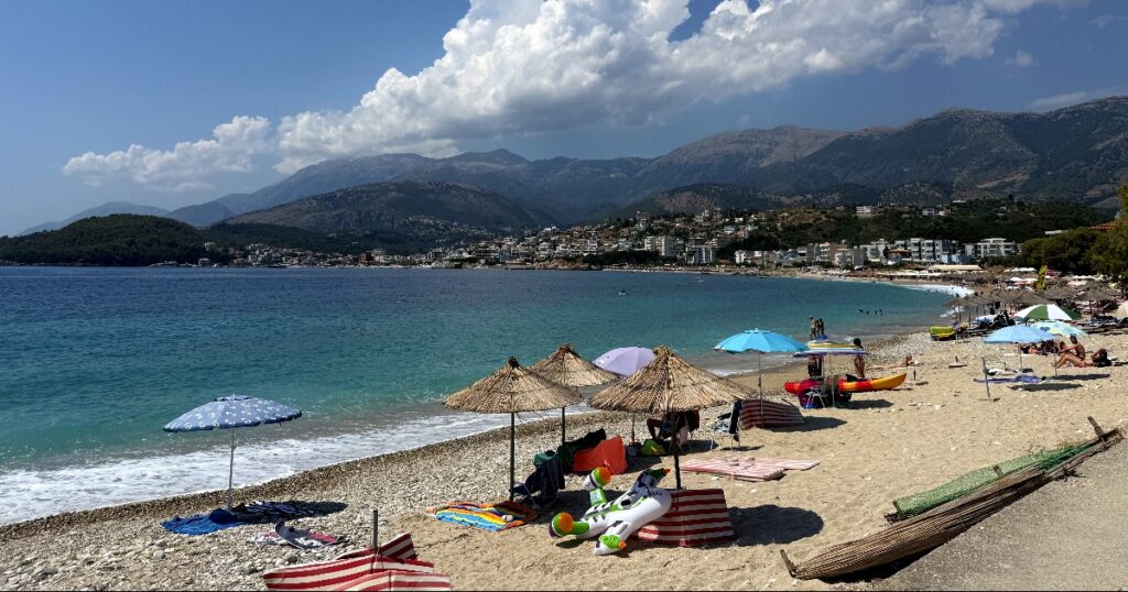 Scenic Albanian coastal beach with mountains, turquoise waters, and beachgoers enjoying the Mediterranean shoreline.