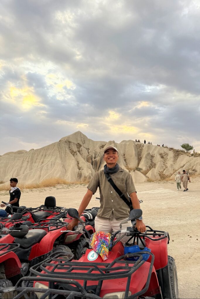 Man on red ATV in Cappadocia's otherworldly badlands landscape with dramatic rock formations.