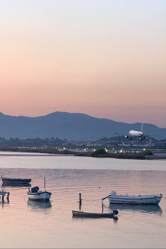 Fishing boats moored in calm waters at dawn with mountains and coastal town in background.