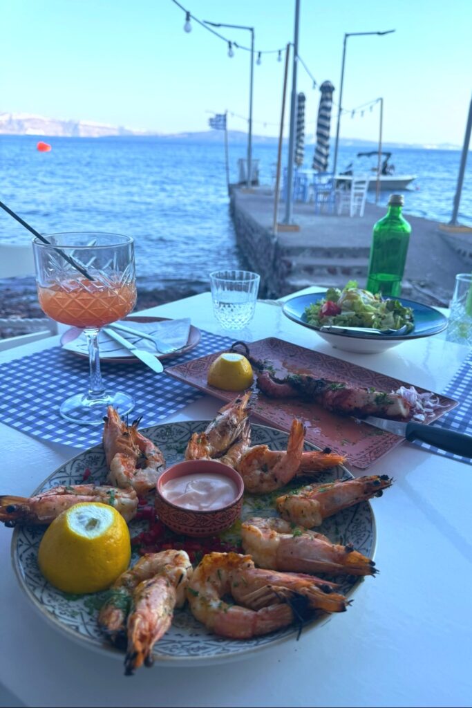 Fresh grilled seafood platter with shrimp and fish at waterfront Greek taverna overlooking harbor in Santorini.