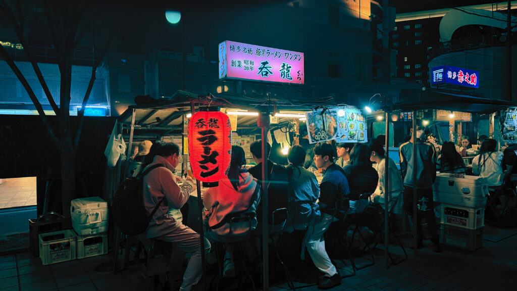 Crowded yatai food stalls illuminated at night in Fukuoka, Japan with red lanterns.