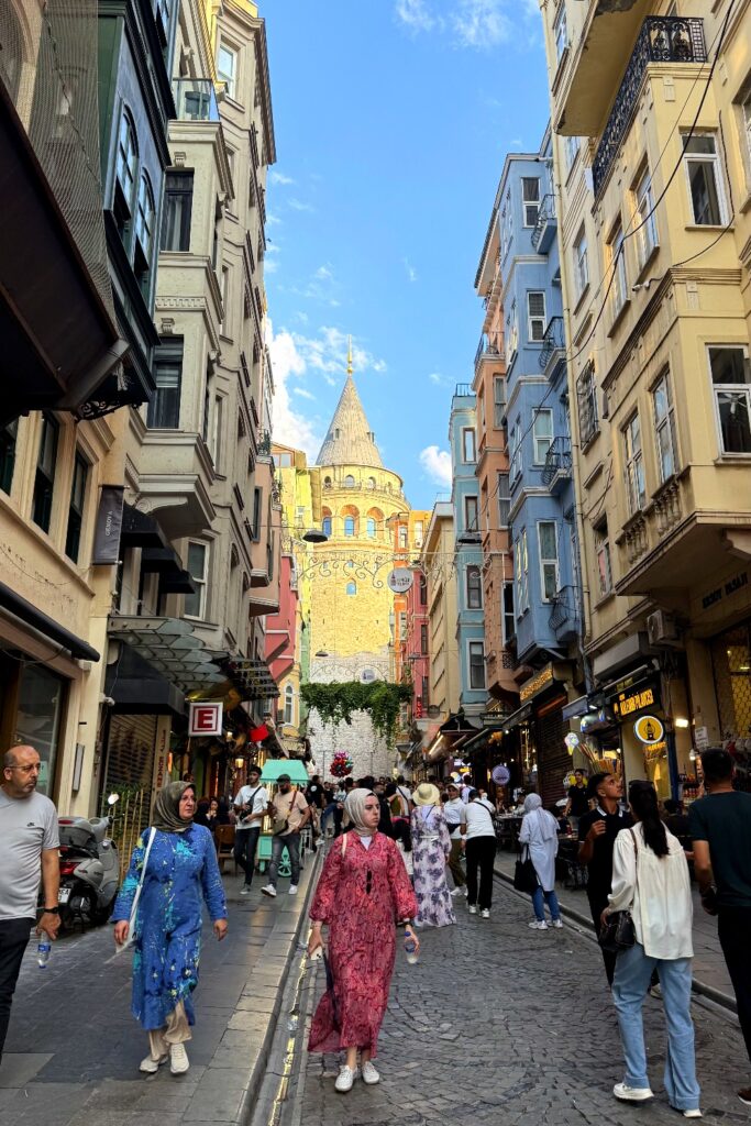 Crowded pedestrian shopping street in Istanbul with Galata Tower visible in the distance.