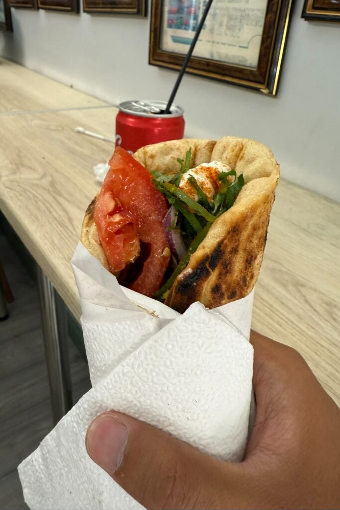 Hand holding wrapped souvlaki with tomatoes and meat in Athens, Greece.