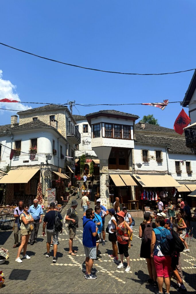 Crowded historic bazaar street with stone buildings and market stalls in Gjirokaster, Albania.
