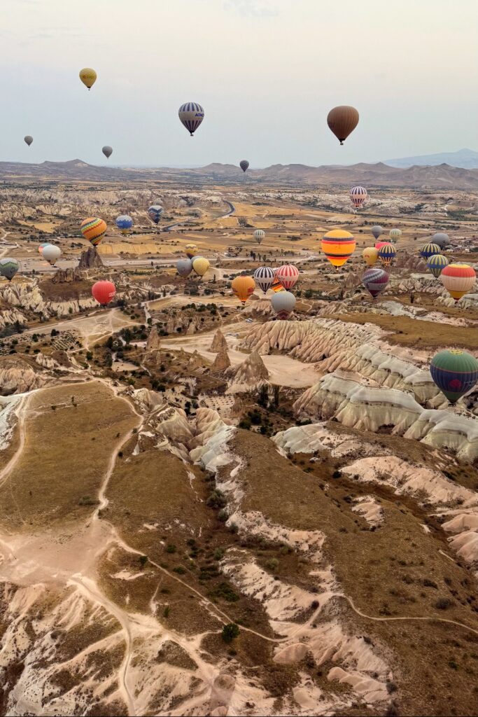 Multiple hot air balloons floating above Cappadocia's distinctive rock formations and landscape.