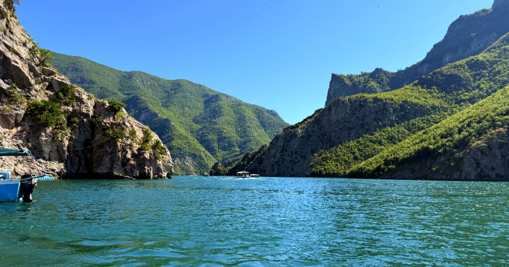 Turquoise waters of Lake Koman surrounded by lush green mountains and dramatic canyon cliffs in Albania.