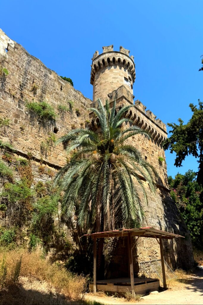 Ancient stone tower with crenellations and palm trees in Rhodes, Greece.