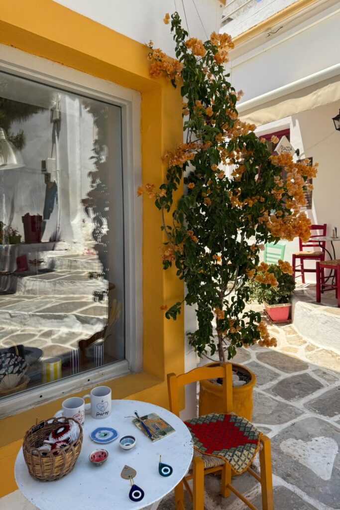 Sunny Greek taverna patio with ivy-covered walls, traditional pottery, and red chairs in Lefkes, Paros.