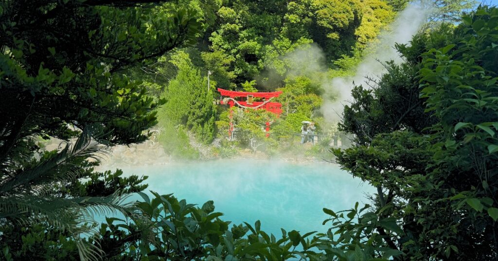 Red bridge spanning turquoise hot spring surrounded by lush green forest at Umi Jigoku, Beppu.