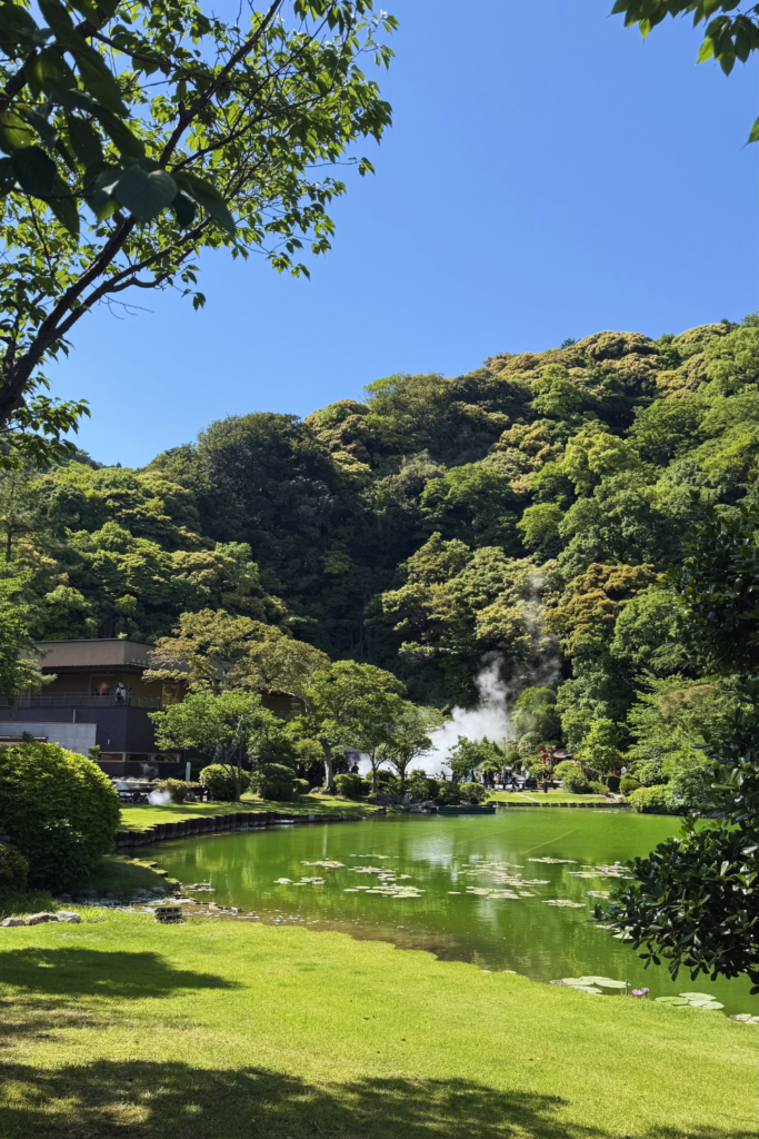 Japanese garden pond with geothermal steam rising from the hillside at Beppu's Jigoku Meguri