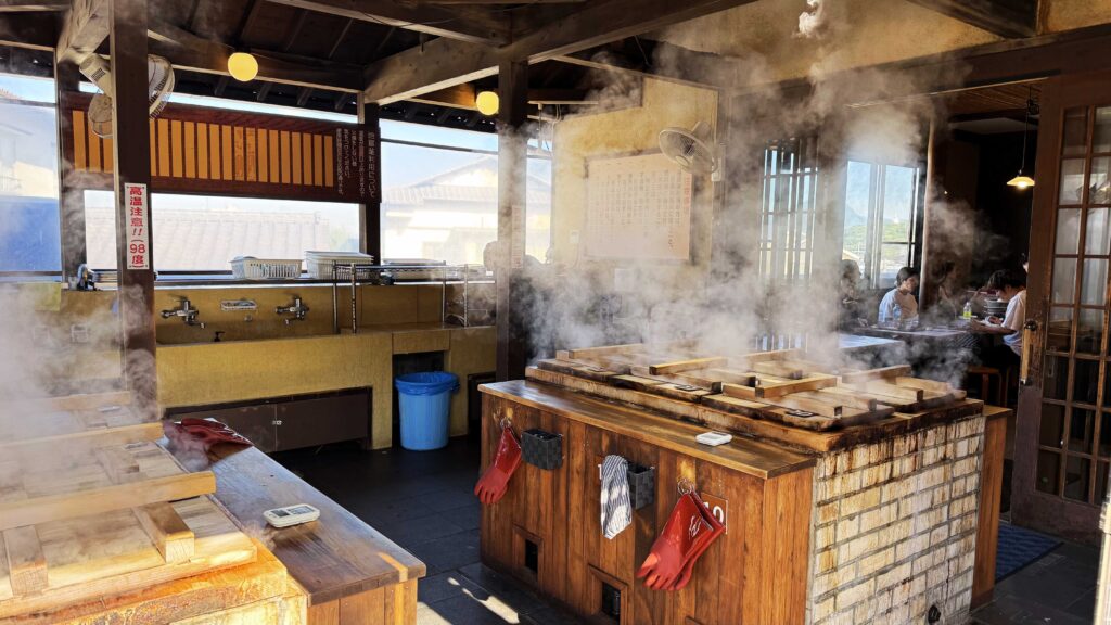 Geothermal steam rising from wooden jigoku-mushi cooking stations at a restaurant in Beppu.