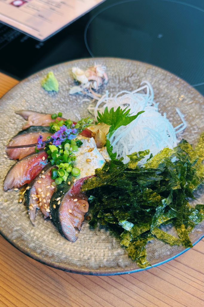 Elegantly plated gomasaba dish featuring raw mackerel slices with seaweed and microgreens.