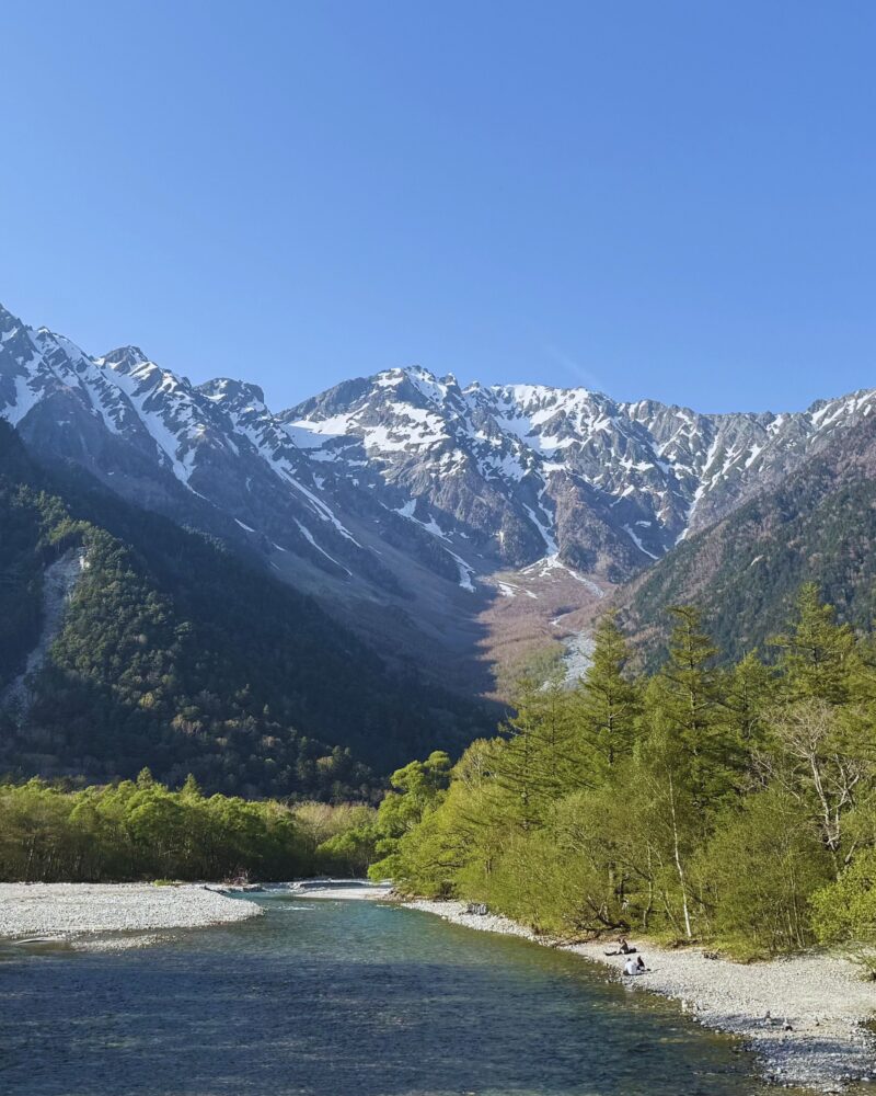 Clear turquoise waters of the Azusa River with Hotaka snow-capped peaks rising above the treeline in Kamikochi