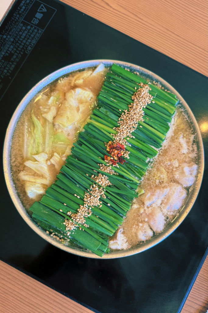 Motsunabe offal hot pot with green onions, sesame seeds, and broth in a ceramic bowl.