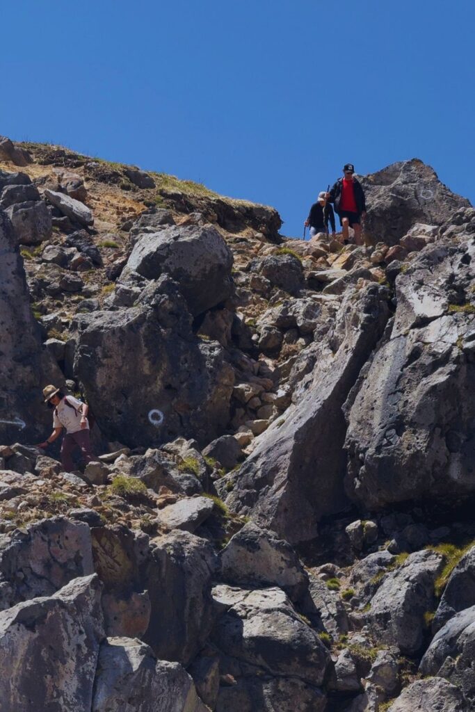 Hikers scrambling over loose rock near the summit of Mount Yakedake in Kamikochi