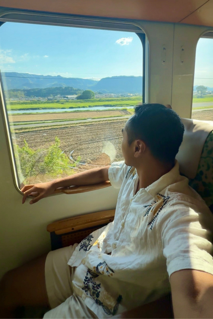 Traveler looking out the window of the Yufuin no Mori train at rural Oita countryside.