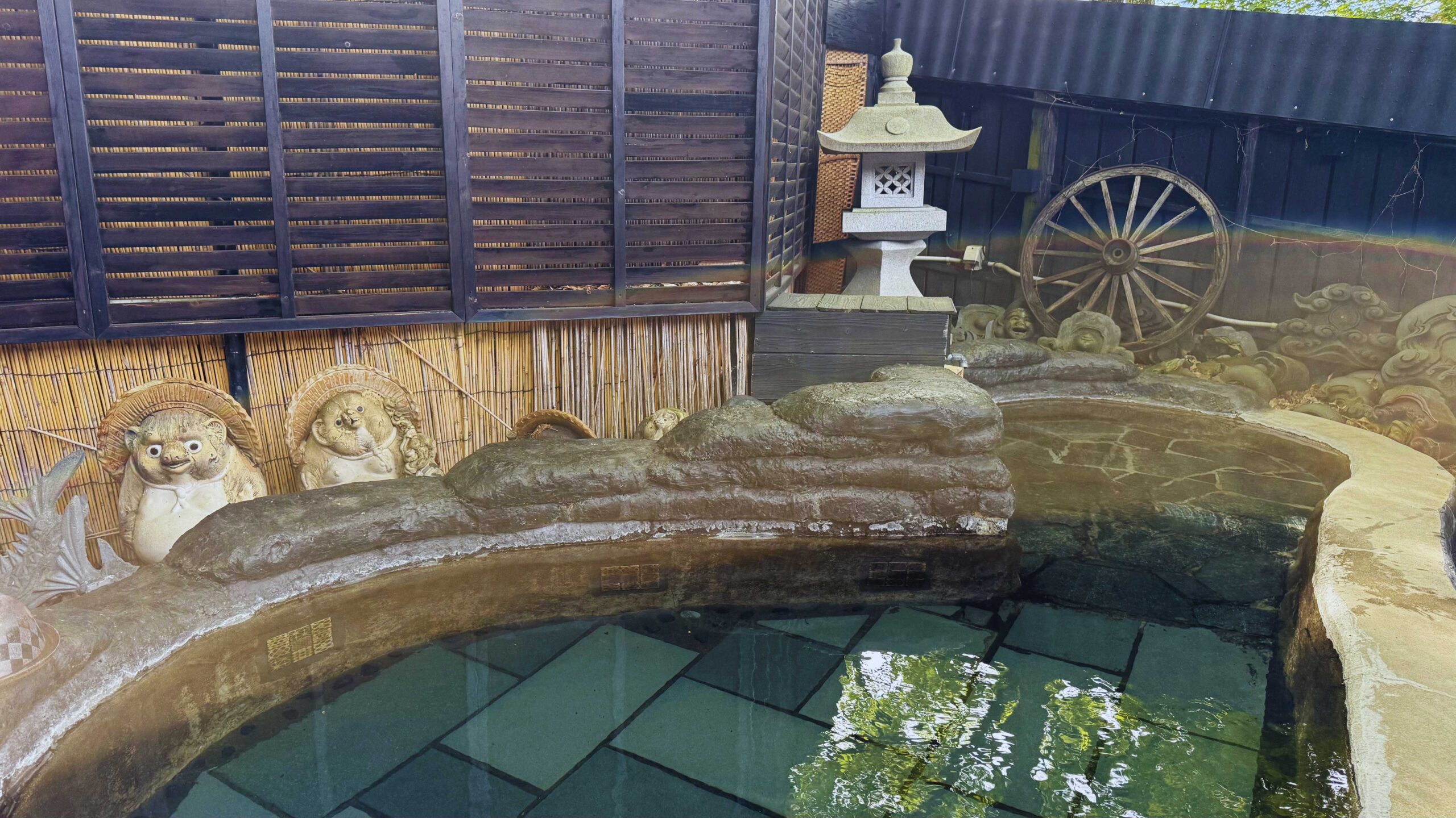 Outdoor rotenburo onsen at a Yufuin ryokan with tanuki statues and a stone lantern.