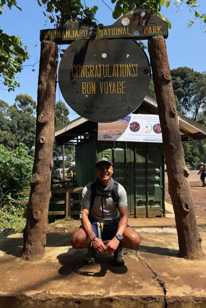 Posing at the Congratulations sign at Mweka Gate after completing the Kilimanjaro descent