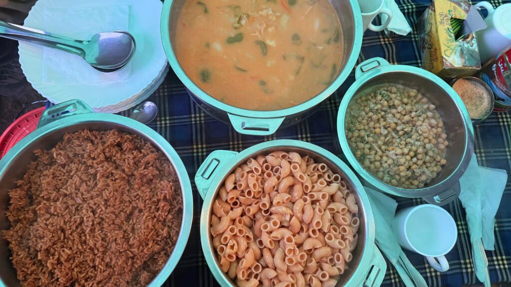 Overhead view of a Kilimanjaro camp meal with pots of rice, macaroni, chickpea stew, and vegetable soup