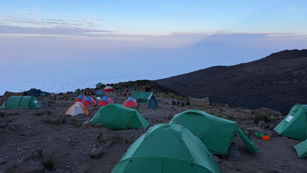 Green tents at a Kilimanjaro camp above a sea of clouds at dusk