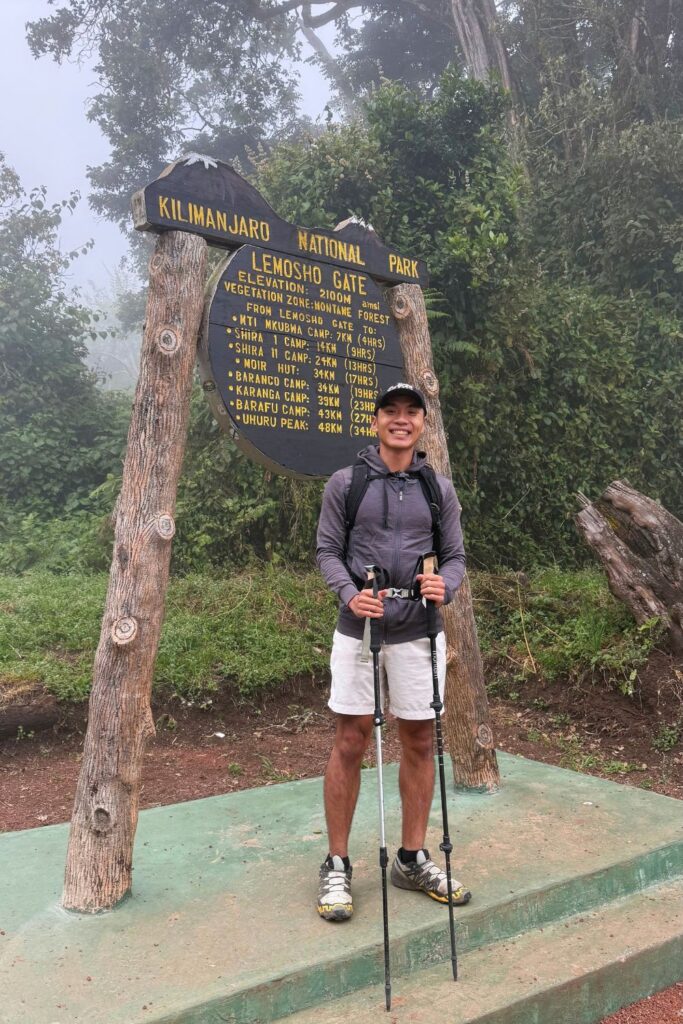 Hiker standing at the Kilimanjaro National Park Lemosho Gate sign, the starting point of the 7-day Lemosho Route