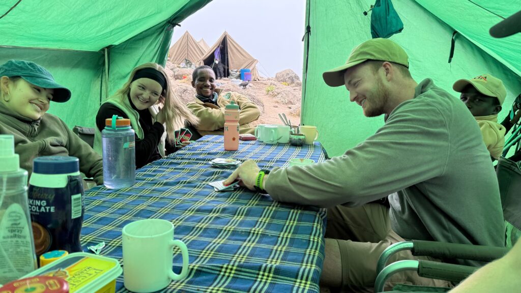 Hikers and guides playing UNO together inside the mess tent at Karanga Camp