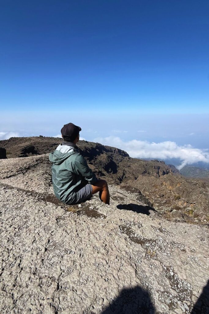 Hiker sitting on a rocky ridge near Kilimanjaro's summit looking out over a sea of clouds