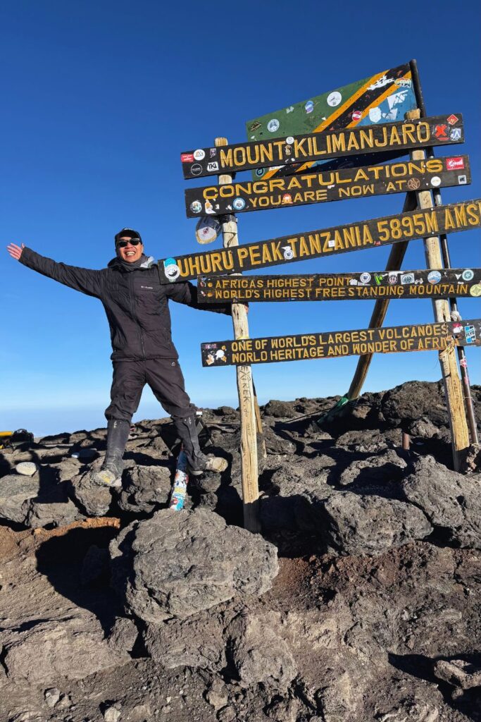 Arms raised in celebration at Uhuru Peak on Mount Kilimanjaro. Climbing Kilimanjaro is one of the biggest contributors to an East Africa trip cost.