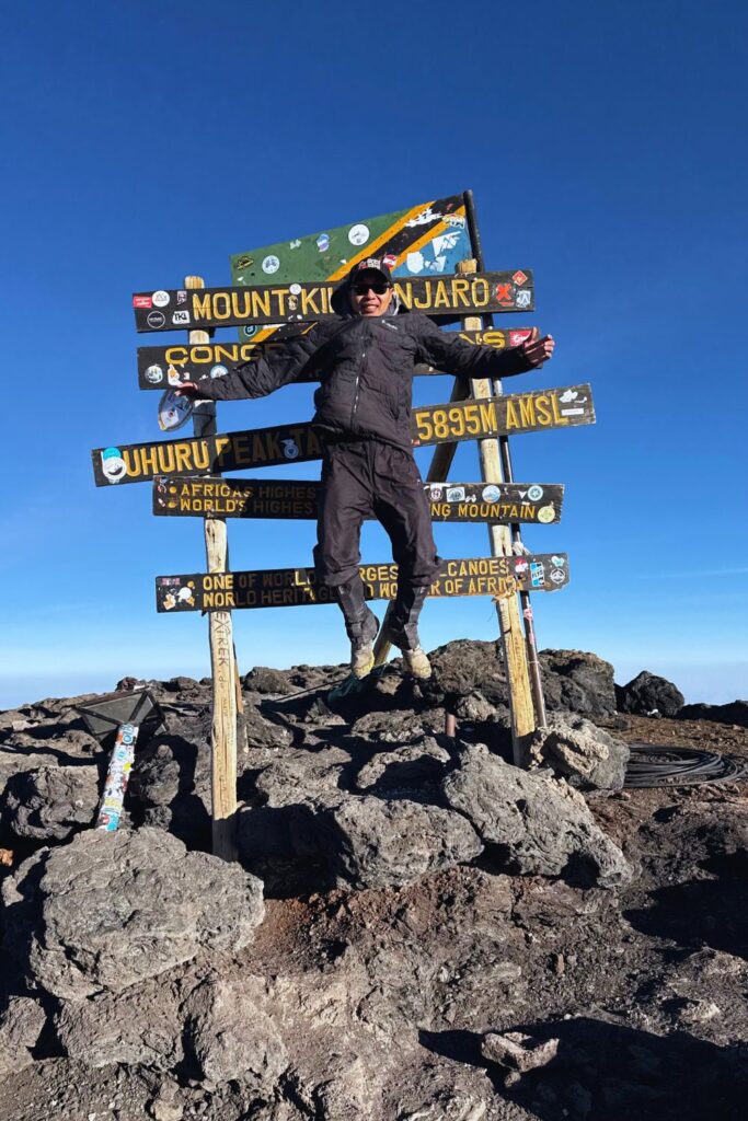 Jumping for joy at the Uhuru Peak summit sign after reaching the top of Kilimanjaro