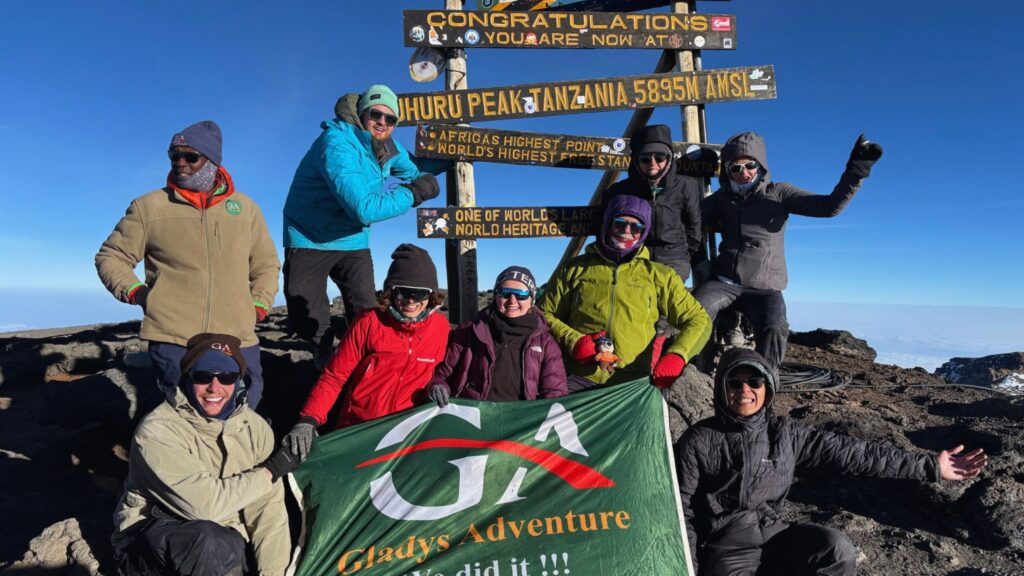 The full hiking group posing at the Uhuru Peak sign, 5895 meters up Kilimanjaro