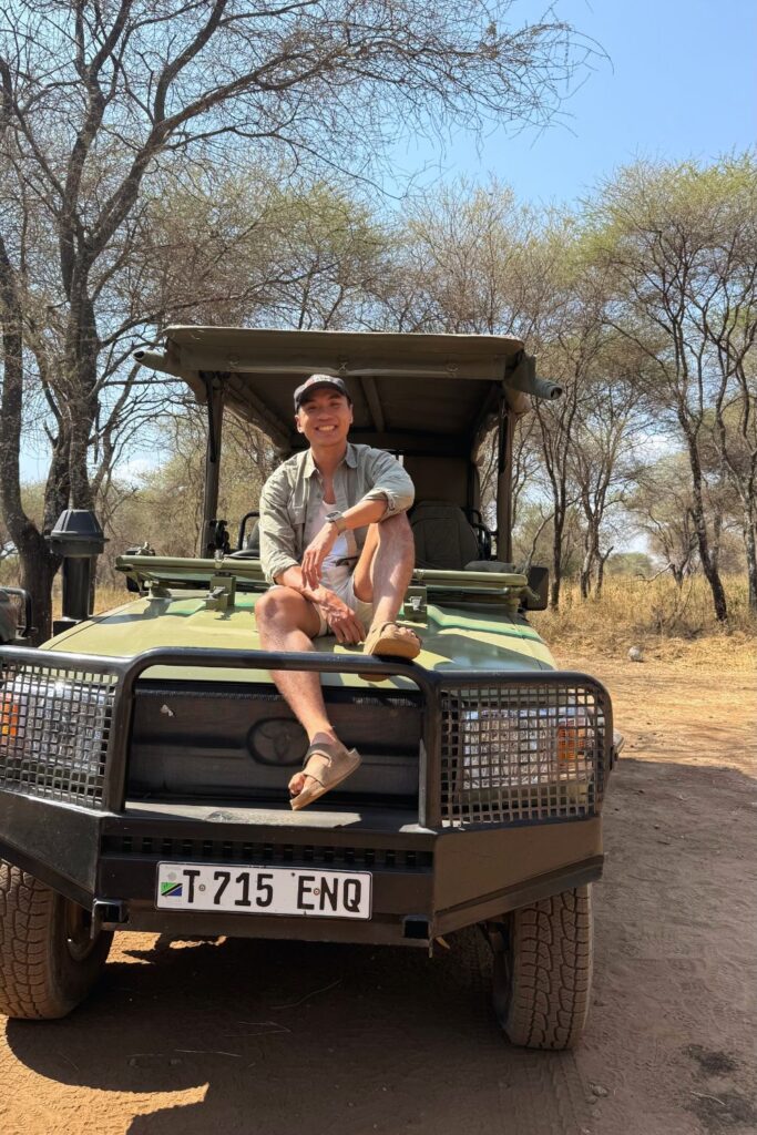 A man sitting on the hood of a safari vehicle during a game drive