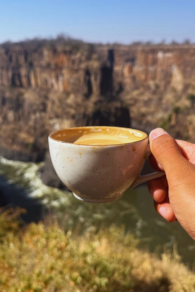 A cappuccino held up in front of Batoka Gorge near Victoria Falls, with cliffs and the Zambezi River below
