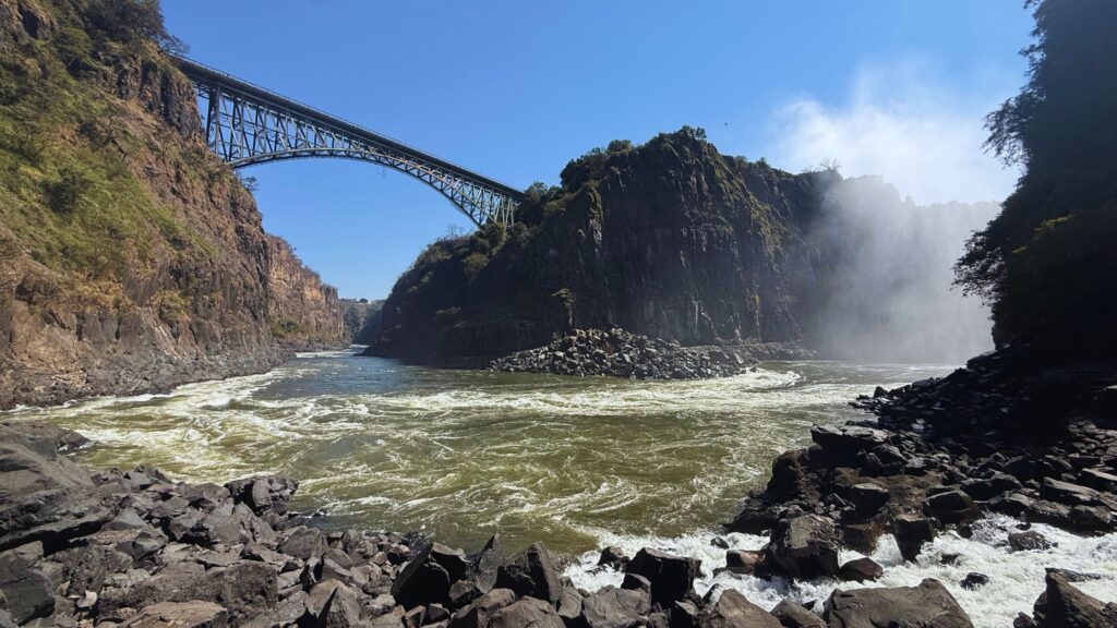 Victoria Falls Bridge seen from the bottom of the gorge, with rapids on the Zambezi and spray rising from the falls