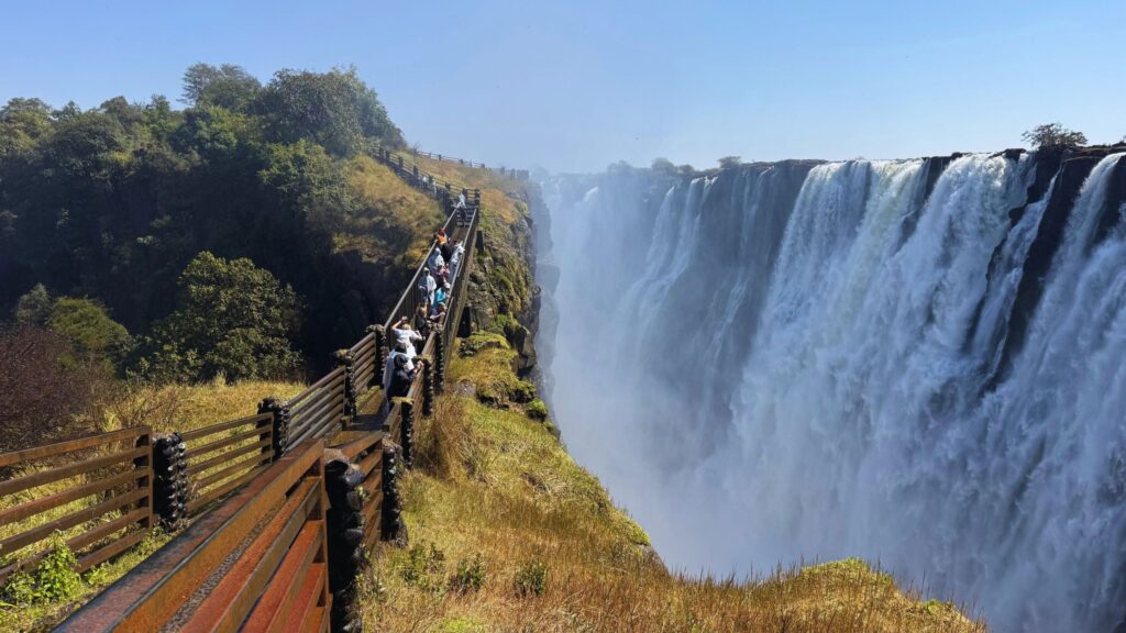 Visitors in raincoats crossing the Knife-Edge Bridge on the Zambia side, with Victoria Falls pouring into the gorge beside them