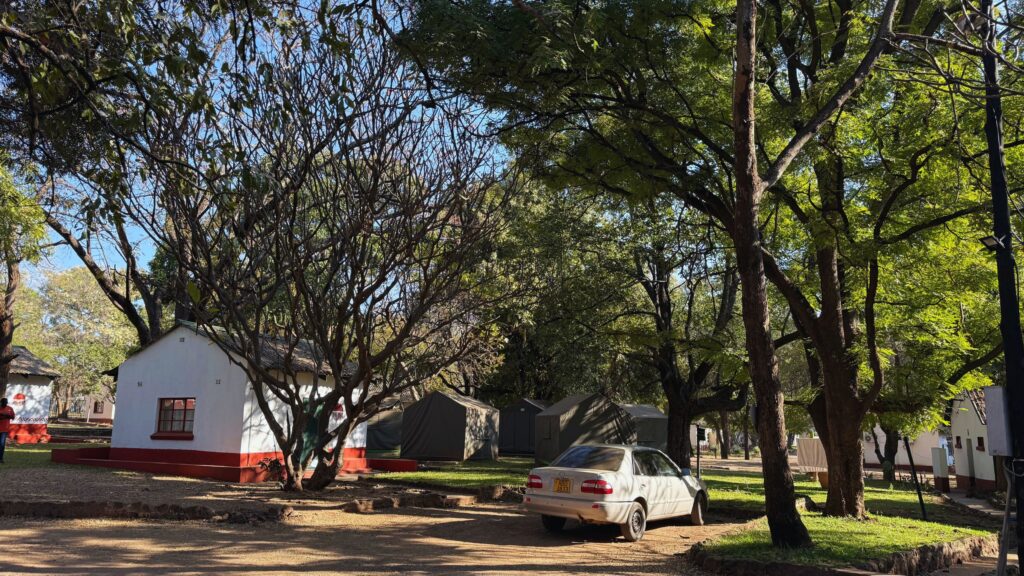 Thatched white chalets with red trim and canvas safari tents under shady trees at Victoria Falls Rest Camp