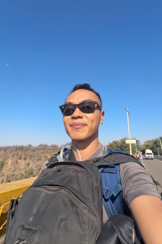 Man wearing a backpack and day pack on Victoria Falls Bridge while crossing the Zambia-Zimbabwe border at Victoria Falls