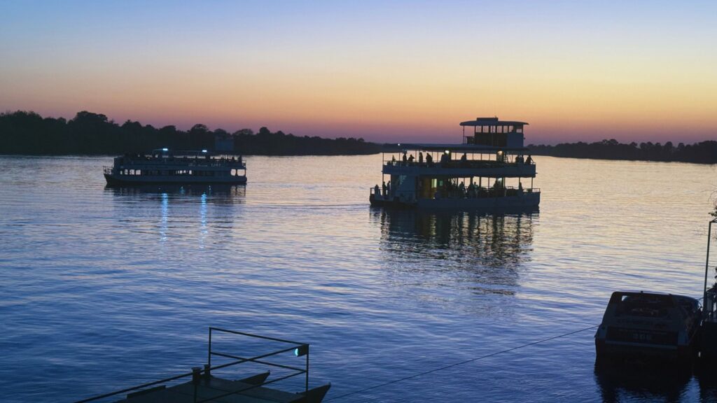 Two double-deck sunset cruise boats in silhouette on the Zambezi River under a purple and orange sky