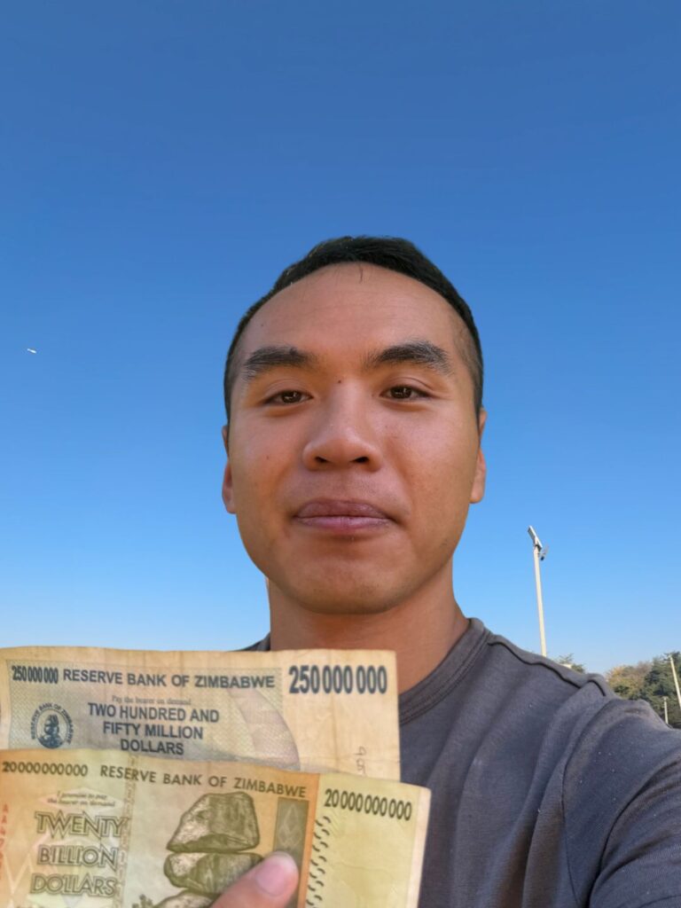 A man holding old Zimbabwe 250 million and 20 billion dollar banknotes in a selfie against a blue sky