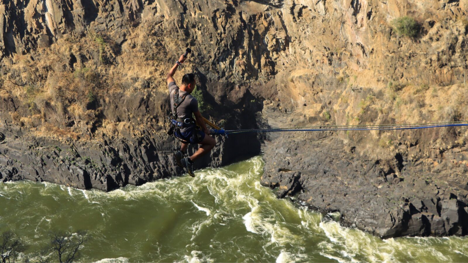 A man mid-jump during a gorge swing over the Batoka Gorge, with whitewater rapids on the Zambezi below